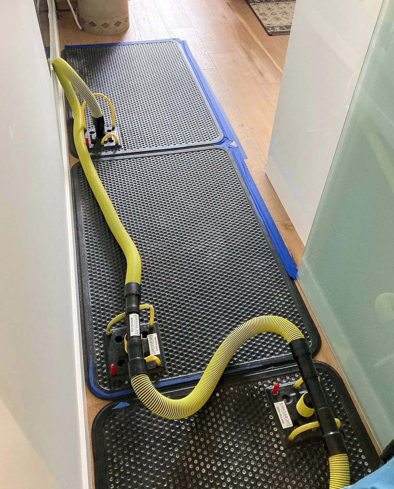 Floor drying mats and hoses set up across a hardwood floor during a Loftin Restoration structural drying job
