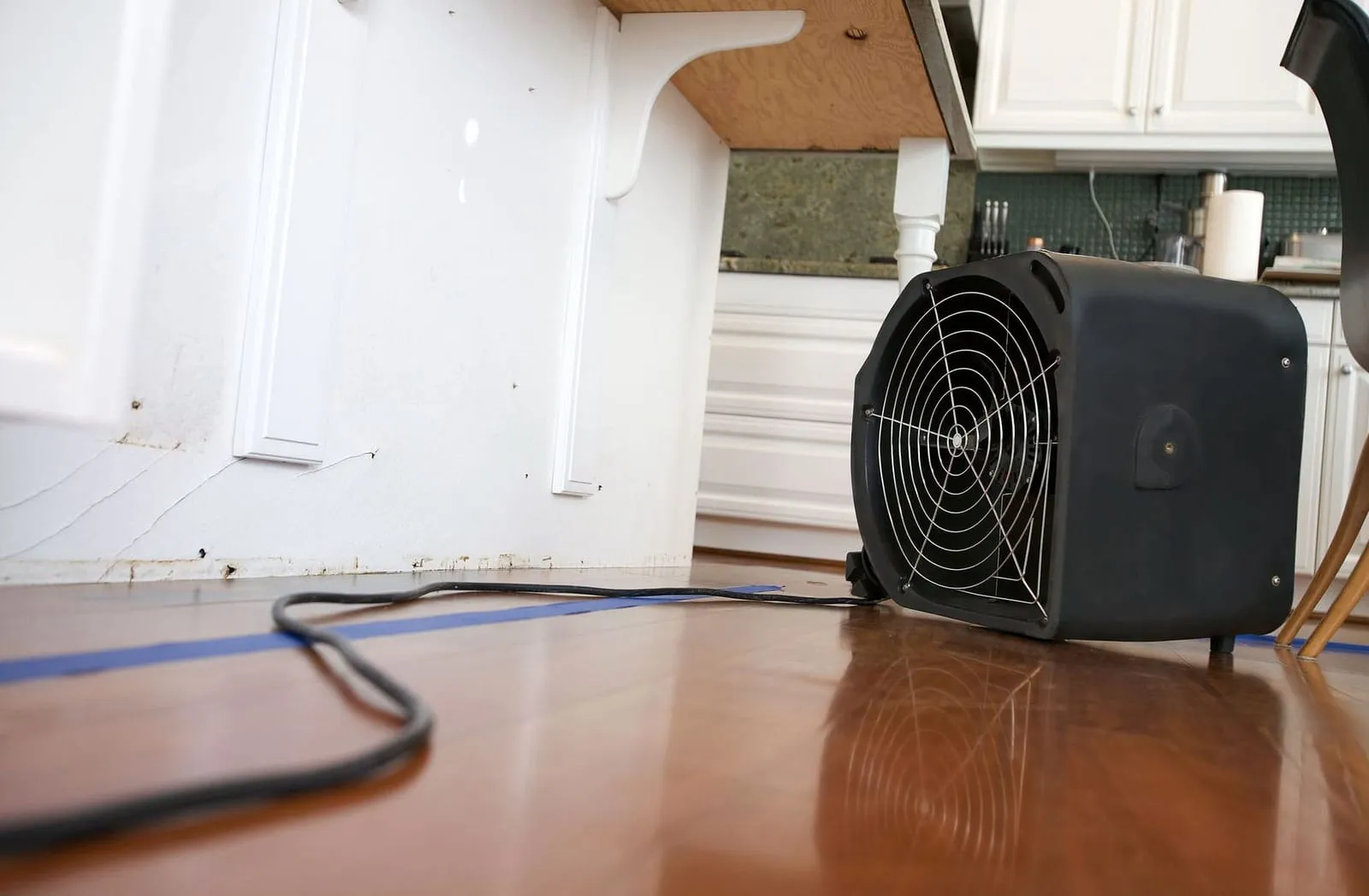 Commercial air mover drying a water-damaged kitchen with lifted baseboards on a Loftin Restoration project